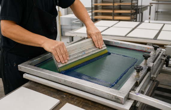 Worker applying ink during silk screen printing in a workshop