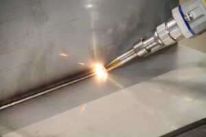 Close-up of a handheld laser welding torch joining stainless steel sheet metal panels with bright sparks