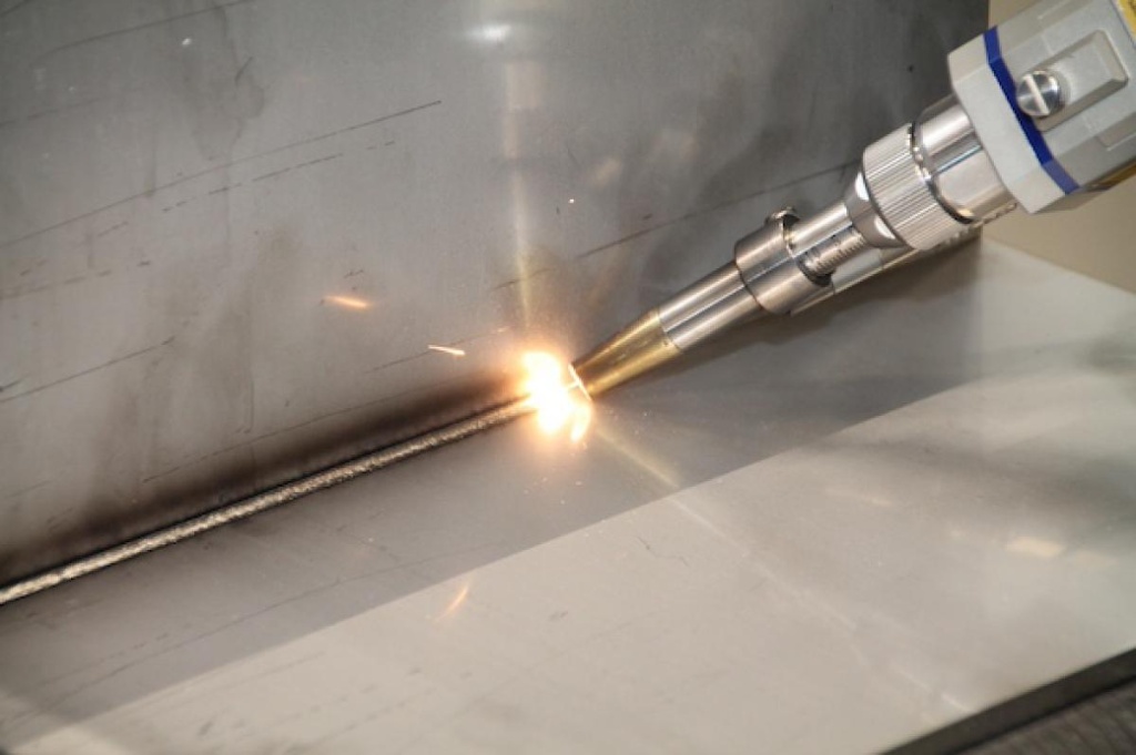Close-up of a handheld laser welding torch joining stainless steel sheet metal panels with bright sparks