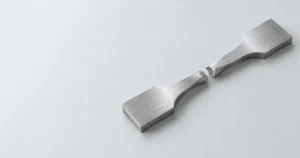 Fractured metal tensile test specimen resting on a clean laboratory surface.