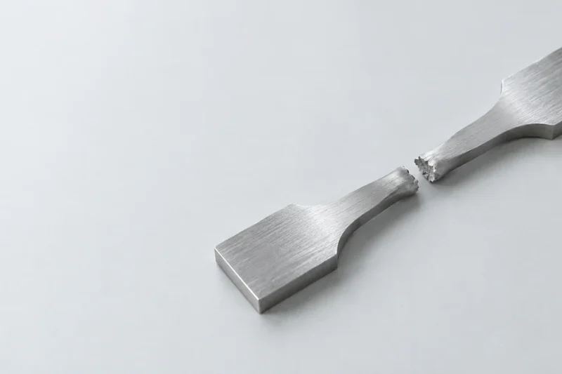 Fractured metal tensile test specimen resting on a clean laboratory surface.